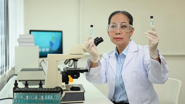 Mature female scientist working analysis with blue liquid test tube in the laboratory.