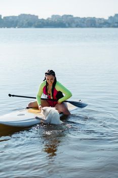 Snow-White Dog Breed Japanese Spitz Swimming in Lake Water and Trying to Get On the Sup Board with Cheerful Woman on It