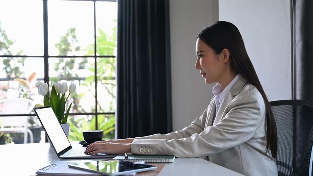 Side view professional businesswoman sitting in bright office and using laptop computer.
