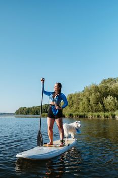 Young Woman with Dreadlocks Standing on Sup Board While Paddleboarding with Her Dog Japanese Spitz