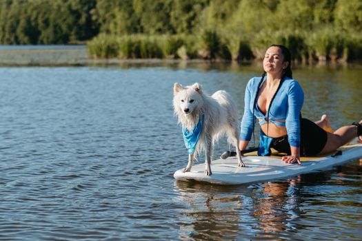 Snowy Japanese Spitz Dog Standing on Sup Board, Woman Doing Stretching While Paddleboarding with Her Pet on City Lake