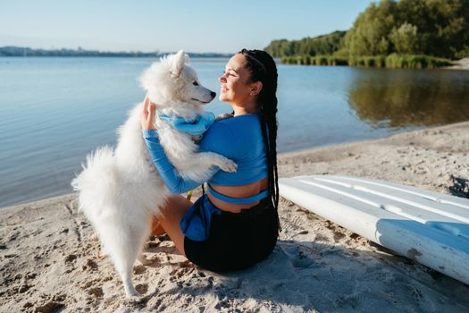 Happy Woman with Dreads Hugging Her Best Friend, Snowy Dog Breed Japanese Spitz, on Beach of City Lake