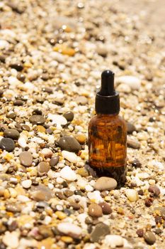Cosmetic serum for the skin in a glass bottle. A bottle with an eyedropper on a pebble beach by the sea. Essences for skin care on the background of stones. The concept of natural cosmetics and SPA products.
