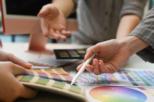 Close up view team of graphic designers working with color swatches and brainstorming for new project at co working space.