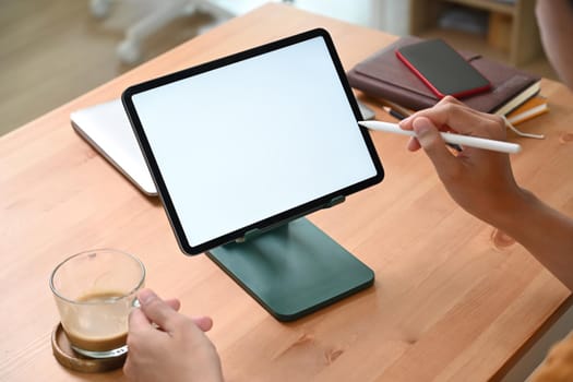 Young man holding coffee cup and using digital tablet in living room.