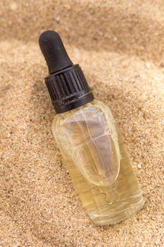 Cosmetic serum for the skin in a glass bottle. A bottle with a pipette on a sandy beach by the sea. Essences for skin care on a sandy background. The concept of natural cosmetics and SPA products.