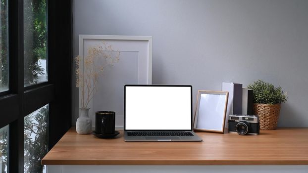 Stylish workplace with laptop computer, picture frame and houseplant.