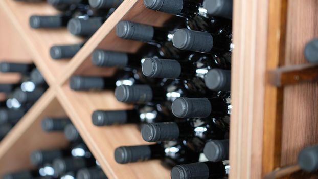 Red wine bottles stacked on wooden racks closeup. Most expensive varieties and brands of wines concept