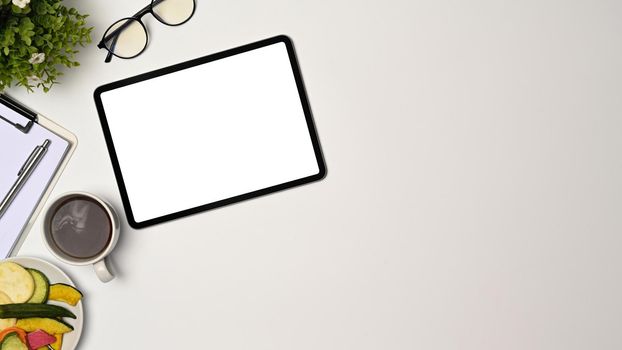 Above view, digital tablet, glasses and coffee cup on white table.