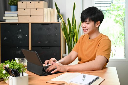 Smiling asian man in casual clothes browsing internet with computer tablet at home.