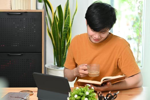 Happy asian man drinking coffee and reading book at home.