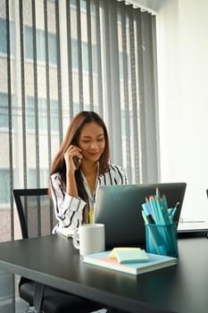 Attractive businesswoman using laptop computer and talking on mobile phone.