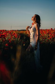 a girl in a white dress walks through a field with poppies at sunset.