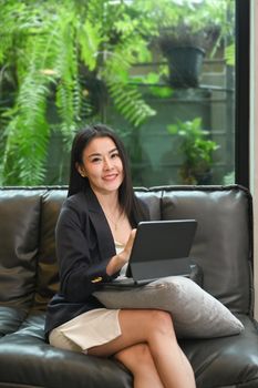 Attractive female entrepreneur sitting on couch in her office and using digital tablet.