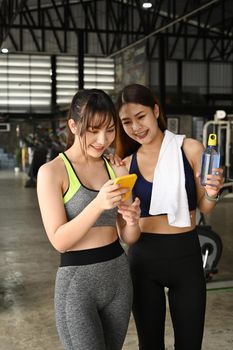 Two fitness women taking rest after exercising at gym and using smart phone.