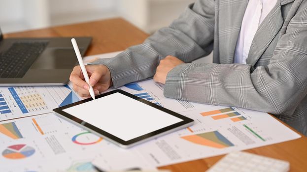 Female investor or economist working with digital tablet and financial graph document at office desk.