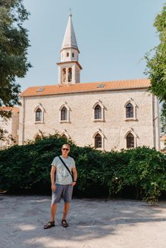 A handsome young man standing and smiling happily in the background of urban buildings. Forty years old caucasian tourist man outdoor near old city buildings - summer holiday.