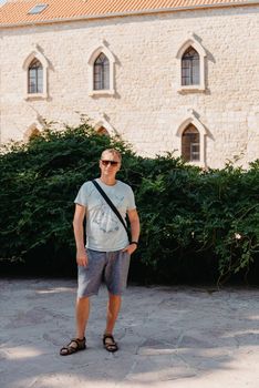 A handsome young man standing and smiling happily in the background of urban buildings. Forty years old caucasian tourist man outdoor near old city buildings - summer holiday.