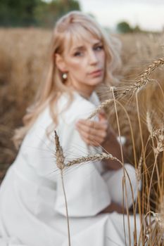 A blonde woman in a long white dress walks in a wheat field. The concept of a wedding and walking in nature.