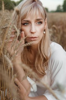 A blonde woman in a long white dress walks in a wheat field. The concept of a wedding and walking in nature.