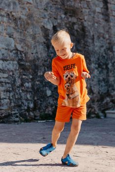 Kid's outdoor activity. Smile toddler boy wearing a orange shorts Jumping, running and having fun in a backyard on a sunny hot summer day. Full length of energetic little boy in stylish casual outfit jumping outdoor