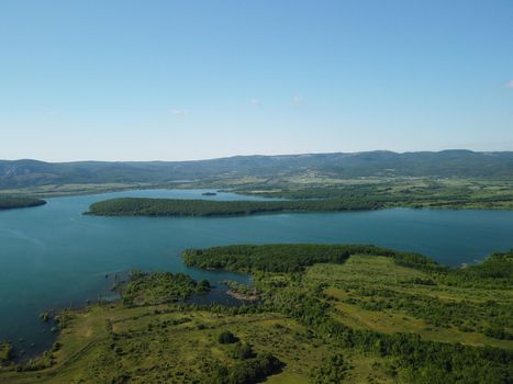 Aerial landscape from flying drone storage reservoir at mountain foot covered colorful spring forest. Beautiful view from above blue lake among highlands