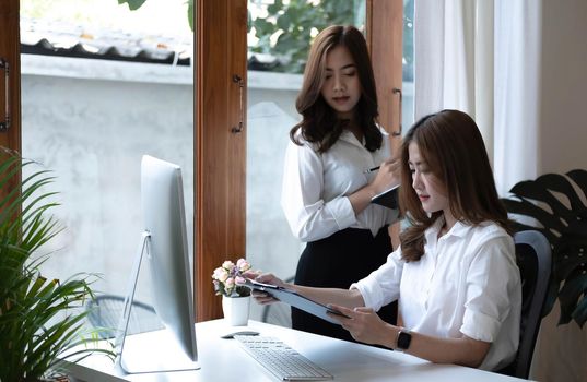 Two young beautiful asian business woman in the conversation, exchanging ideas at work..