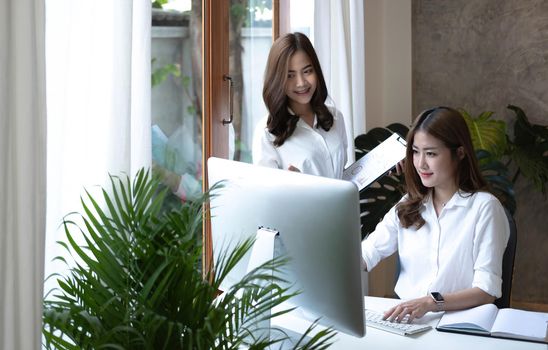 Two young Asian businesswoman discuss investment project working and planning strategy. Business people talking together with laptop computer at office..