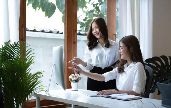 Two young Asian businesswoman discuss investment project working and planning strategy. Business people talking together with laptop computer at office..