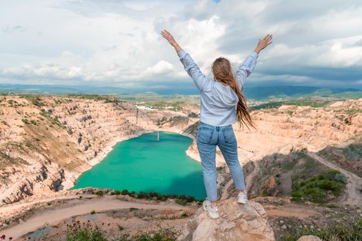 Girl on top of a mountain with raised hands, view of the azure lake in the form of a heart behind.