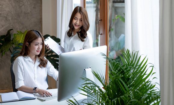 Two young Asian businesswoman discuss investment project working and planning strategy. Business people talking together with laptop computer at office..