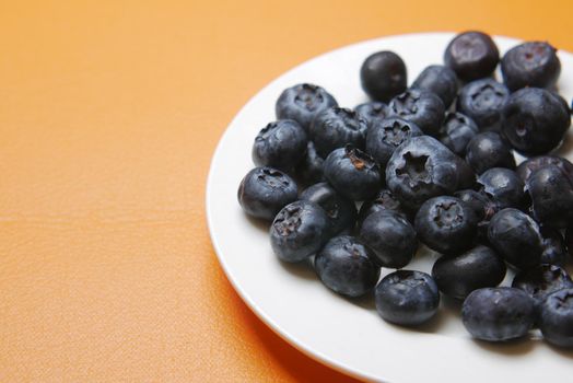 Close up of fresh blue berry on a plate on orange background ,