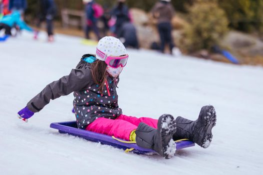 A young girl tobogganing at Lake Mountain on a clear sunny day in Victoria, Australia