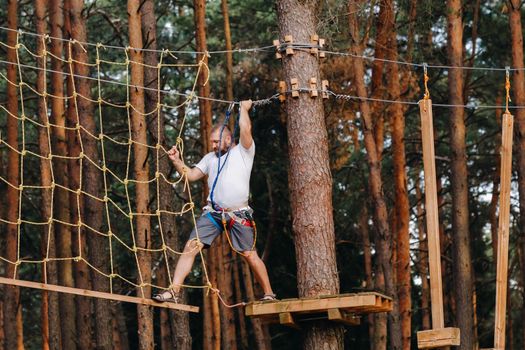 A man overcomes an obstacle in a rope town. A man in a forest rope park.