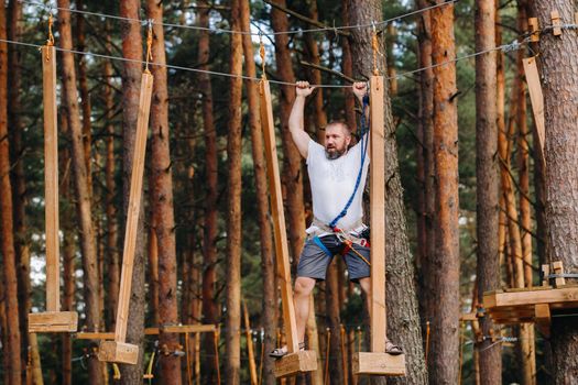 A man overcomes an obstacle in a rope town. A man in a forest rope park.