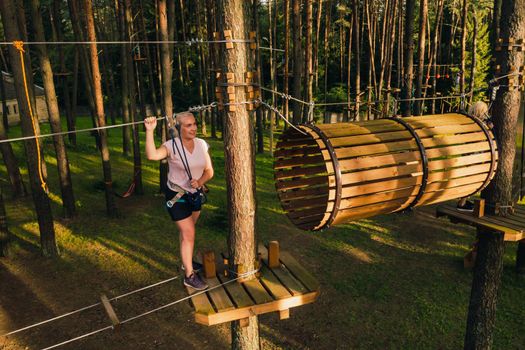 A woman overcomes an obstacle in a rope town. A woman in a forest rope park.