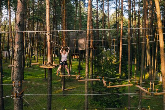 A woman overcomes an obstacle in a rope town. A woman in a forest rope park.