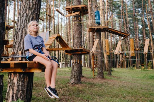 A girl passes an obstacle in a rope town. A girl in a forest rope park.