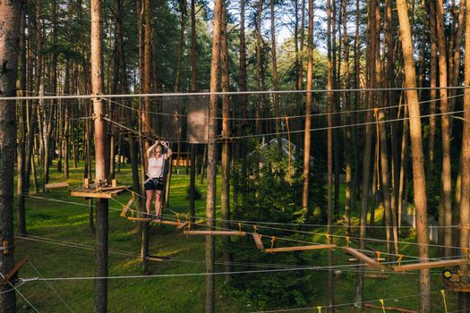 A woman overcomes an obstacle in a rope town. A woman in a forest rope park.