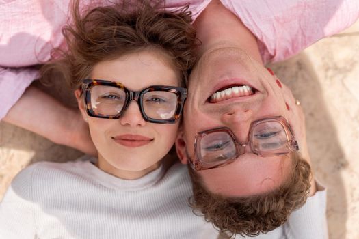 Portrait of two attractive students man and woman wearing stylish glasses lying on floor outdoor and smiling, head to head cheek to cheek, break relax between lesson, work, projects Eyeglasses concept