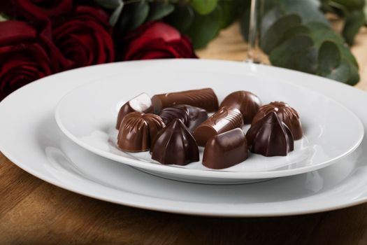 Plate of chocolates close up with roses in the background