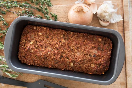 Vegan lentil loaf in baking pan on cutting board with some ingredients, view from above