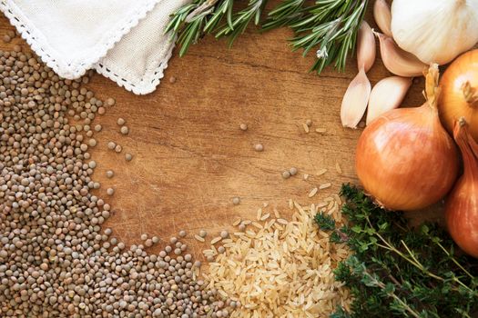 Healthy food frame with fresh vegetables, herbs and grains on rustic wooden background viewed from above.