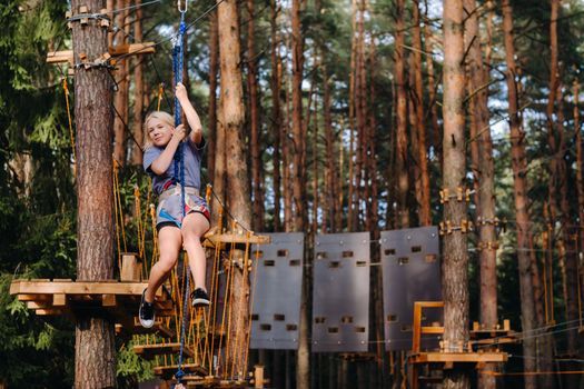 A girl passes an obstacle in a rope town. A girl in a forest rope park.