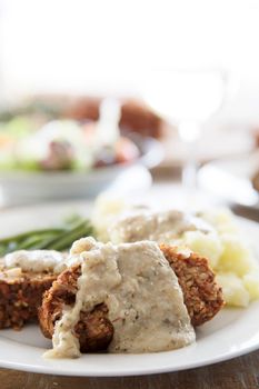 Slices of vegan lentil loaf covered in gravy with mashed potatoes and green beans. Vertical orientation.
