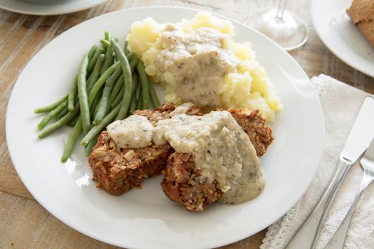 Slices of vegan lentil loaf with mashed potatoes and green beans.