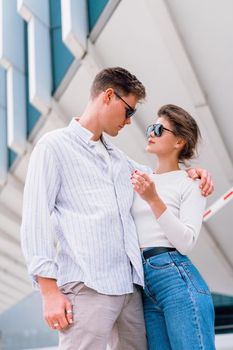 Smiling beautiful woman and her handsome boyfriend. Woman in casual summer jeans. Happy cheerful couple in sunglasses walking business district. Couple posing on the street modern building background