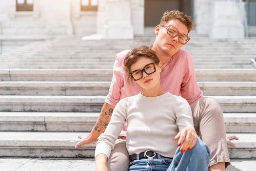 Young beautiful hipster couple in love sitting stairs on old city street, summer Europe vacation, travel, fun, happy, smiling, glasses, trendy outfit, romance, date, embracing