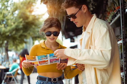 Tourist Couple With Map In Capital City Europe. Happy Young People Using Map, Traveling On Summer Vacations. Handsome Man And Beautiful Woman Having Trip Outdoors. High Quality Image.