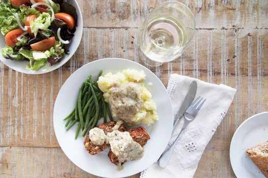 Slices of vegan lentil loaf covered in gravy with mashed potatoes and green beans, flat lay.